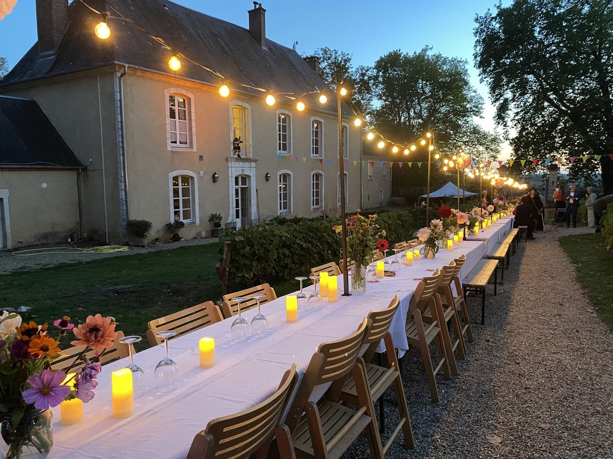 Une longue table dressée devant la maison, un soir d’été, sous les guirlandes